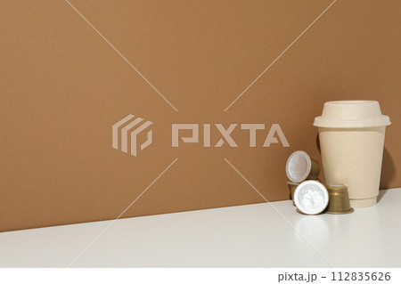 Coffee capsules and paper cup on brown background, space for text 112835626