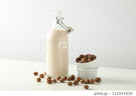Bottle with milk and bowls with nuts on white background 112835630