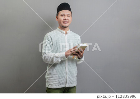 Asian Muslim man holding prayer beads and reading Qur'an Asian Muslim man holding prayer beads and reading Qur'an 112835996