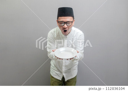 Happy asian muslim man holding empty white plate or dish 112836104