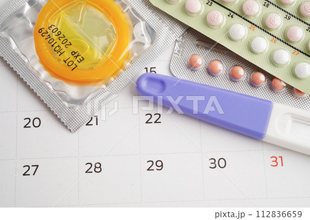 Pregnancy test with birth control pills and condom for female on calendar, ovulation day. Pregnancy test with birth control pills and condom for female on calendar, ovulation day. 112836659