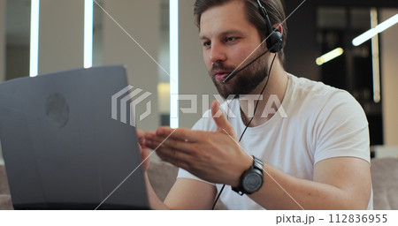 Young man sitting at home wear wireless headset having video conference. Concept of remote work or education. 112836955