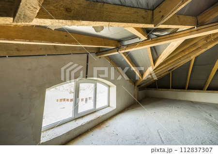 Attic of a building with wooden beams of a roof structure and a small window. 112837307