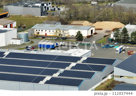 Aerial view of solar power plant with blue photovoltaic panels mounted on industrial building roof for producing green ecological electricity. Production of sustainable energy concept Aerial view of solar power plant with blue photovoltaic panels mounted on industrial building roof for producing green ecological electricity. Production of sustainable energy concept 112837444