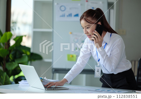 Young asian business woman talk on smartphone write notebook laptop in office. Startup business woman online sme telemarketing Young asian business woman talk on smartphone write notebook laptop in office. Startup business woman online sme telemarketing 112838551