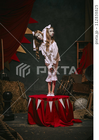 Siamese twin girls in white vintage costumes with makeup standing over dark retro circus backstage background. Creative spooky play 112838825