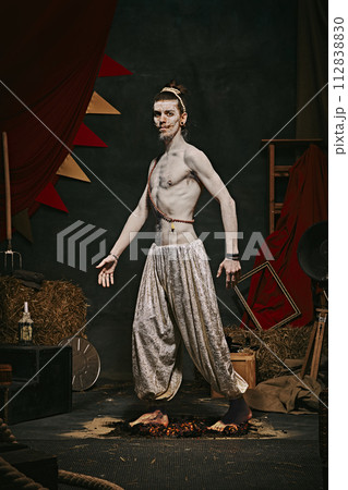 Pale man with muscular shirtless body, yogi male circus performance over dark retro circus backstage background. Pale man with muscular shirtless body, yogi male circus performance over dark retro circus backstage background. 112838830