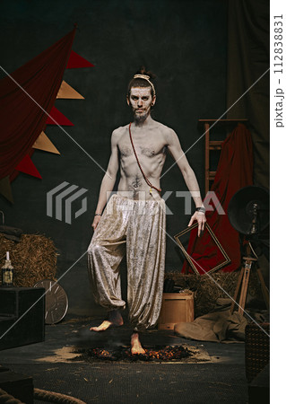 Pale man with muscular shirtless body, yogi male circus performance over dark retro circus backstage background. Pale man with muscular shirtless body, yogi male circus performance over dark retro circus backstage background. 112838831