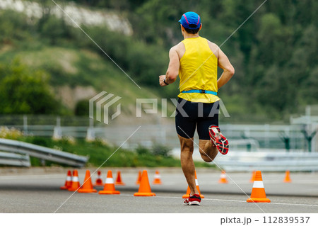 rear view athlete running on asphalt with orange safety cones, mountain marathon race 112839537