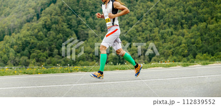 man athlete athlete running in background of green forest, compression sleeves on legs 112839552
