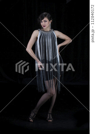 A beautiful girl dressed in the style of the 20-30s of the last century posing on a dark background. 112840172