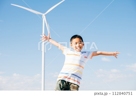 A portrait of a happy boy amidst a wind farm. Joyful family time in nature's embrace embracing clean energy and playful moments near windmills. Smiling child enjoying nature's escape. 112840751