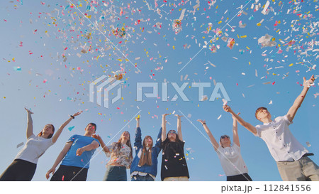 Friends toss colorful paper confetti from their hands. Friends toss colorful paper confetti from their hands. 112841556