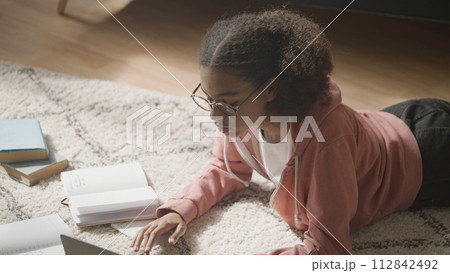 Smart schoolgirl lying on floor at home, working on laptop, preparing for test Smart schoolgirl lying on floor at home, working on laptop, preparing for test 112842492