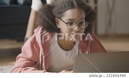 Smiling black teenage girl in eyeglasses having video call on laptop, distance education 112842494