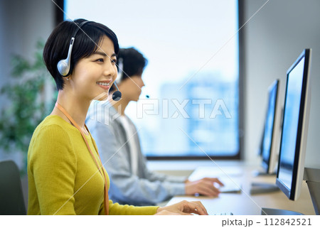 オフィスでヘッドセットをつけて対応するオペレーターの女性 オフィスでヘッドセットをつけて対応するオペレーターの女性 112842521