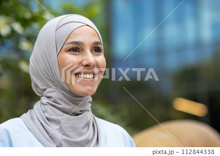 Elegant and modern young woman wearing a hijab against an urban backdrop, exuding confidence and style. 112844338