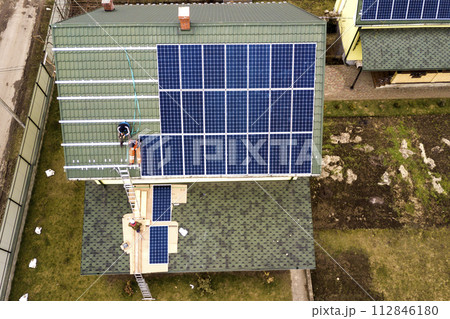 Aerial top view of residential house with team of workers installing solar photo voltaic panels system on roof. Renewable energy production concept. 112846180