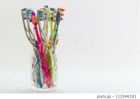 Close up shot of set of multicolored toothbrushes in glass on clean toilet on white background, concept dental. Close up shot of set of multicolored toothbrushes in glass on clean toilet on white background, concept dental. 112846181