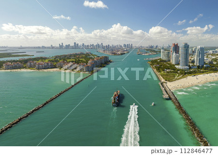 View from above of big container ship entering main channel in Miami harbor near South Beach high luxurious hotels and apartment buildings View from above of big container ship entering main channel in Miami harbor near South Beach high luxurious hotels and apartment buildings 112846477