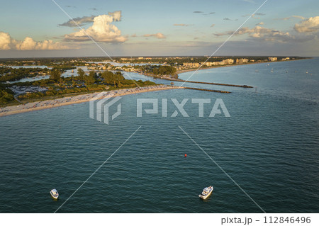 Aerial view of sea shore near Venice, Florida with white yachts at sunset floating on sea waves. North and South Jetty on Nokomis beach. Motor boat recreation on ocean surface 112846496
