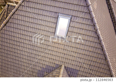 Close-up of new attic plastic window installed in shingled house roof. Professionally done building and construction work, roofing and installation concept. 112846563