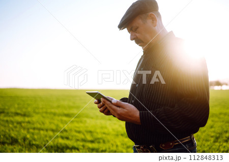 Farmer owner using touchpad for check wheat field at sunset. Farmer working with digital tablet. Farmer owner using touchpad for check wheat field at sunset. Farmer working with digital tablet. 112848313