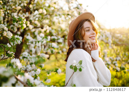 Smiling woman with hat posing in blooming spring park. Concept of relax, travel, spring vacation. Smiling woman with hat posing in blooming spring park. Concept of relax, travel, spring vacation. 112848617