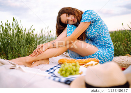 Young woman sits on a plaid with a book. Summer picnic in nature. Healthy food. Young woman sits on a plaid with a book. Summer picnic in nature. Healthy food. 112848687