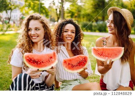 Cheerful happy friends camping on the grass, eating watermelon, laughing. Cheerful happy friends camping on the grass, eating watermelon, laughing. 112848829