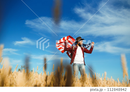 4th of July. American Flag. Traveler with the flag of America. The man in a hat, a backpack, a shirt and jeans. 112848942