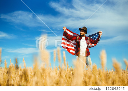 4th of July. American Flag. Traveler with the flag of America. The man in a hat, a backpack, a shirt and jeans. 4th of July. American Flag. Traveler with the flag of America. The man in a hat, a backpack, a shirt and jeans. 112848945