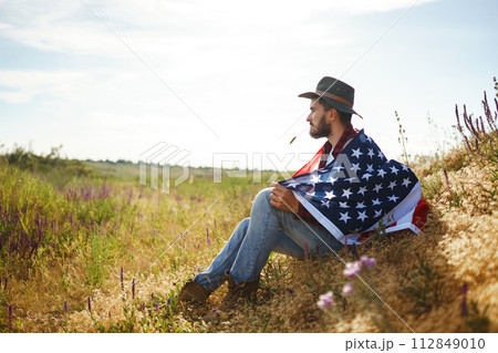 4th of July. American Flag. Traveler with the flag of America. The man in a hat, a backpack, a shirt and jeans. 4th of July. American Flag. Traveler with the flag of America. The man in a hat, a backpack, a shirt and jeans. 112849010