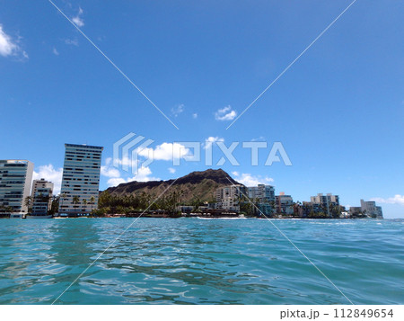 Waikiki Waves lap towards seawall, with coconut trees, Condo buildings, and Diamond Head Crater in the distance 112849654