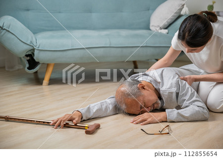 Dizziness elderly old man falling down lying on floor with walking stick and assistant nurse help to support, senior father fall on the ground and his daughter helping wake up and get up, accident 112855654