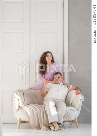 Young happy couple sitting on a sofa in a large studio. Behind them is a large white door. Loving married couple. Cope space for text 112857541