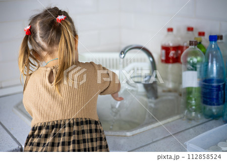 A child sorts plastic bottles in the kitchen. A little girl painstakingly puts plastic into containers for recycling. A family of environmental activists sorts garbage and fights to save the planet. A child sorts plastic bottles in the kitchen. A little girl painstakingly puts plastic into containers for recycling. A family of environmental activists sorts garbage and fights to save the planet. 112858524