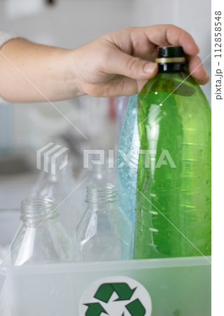 Vertical. A woman's hand puts a plastic bottle into a box with a recycling sign. Close-up. Female hands sort plastic into boxes for recycling. The concept of recycling household waste. Vertical. A woman's hand puts a plastic bottle into a box with a recycling sign. Close-up. Female hands sort plastic into boxes for recycling. The concept of recycling household waste. 112858548