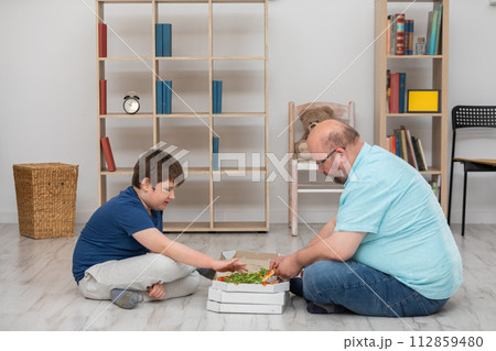 Sitting on the floor, father and son pick out slices of pizza. 112859480