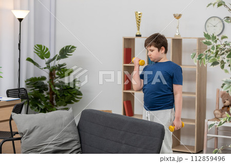 A young boy trains with dumbbells for health. A young boy trains with dumbbells for health. 112859496
