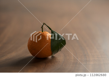 Small organic tangerine with leaves on wood table 112862680