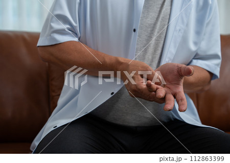 Elderly Asian male patients suffer from numbing pain in hands from rheumatoid arthritis. Senior men massage his hand with wrist pain. Concept of joint pain, rheumatoid arthritis, and hand problems. 112863399
