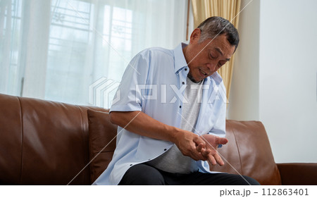 Elderly Asian male patients suffer from numbing pain in hands from rheumatoid arthritis. Senior men massage his hand with wrist pain. Concept of joint pain, rheumatoid arthritis, and hand problems. 112863401