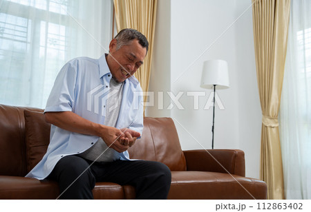 Elderly Asian male patients suffer from numbing pain in hands from rheumatoid arthritis. Senior men massage his hand with wrist pain. Concept of joint pain, rheumatoid arthritis, and hand problems. 112863402
