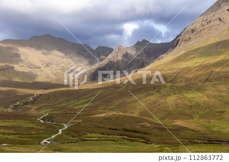 Meandering path through Isle of Skye verdant valley leading to Fairy Pools under a dramatic sky Meandering path through Isle of Skye verdant valley leading to Fairy Pools under a dramatic sky 112863772