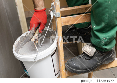 A close up shows how a manual worker soaks a paint roller in a bucket with moisture insulation. Protective glove. A close up shows how a manual worker soaks a paint roller in a bucket with moisture insulation. Protective glove. 112864577
