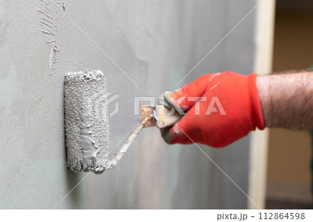 A close-up view of an experienced construction worker applying damp insulation using a paint roller on a wall. 112864598