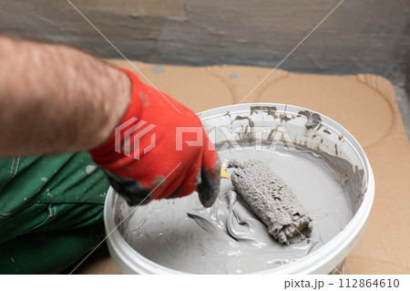 A close up shows how a manual worker soaks a paint roller in a bucket with moisture insulation. Protective glove. A close up shows how a manual worker soaks a paint roller in a bucket with moisture insulation. Protective glove. 112864610