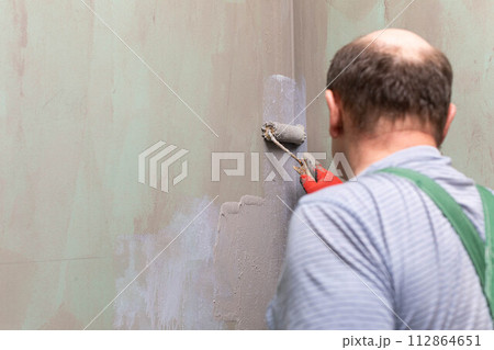 In the bathroom, a general construction worker applies moisture insulation using a roller. 112864651