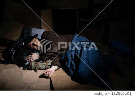 A homeless middle-aged man sleeps in cardboard boxes outside. A homeless middle-aged man sleeps in cardboard boxes outside. 112865101